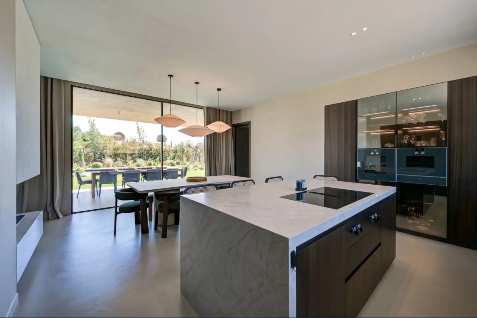 Cuisine de la Villa F. à Éguilles : îlot en pierre, façades sombres et baies sur le jardin