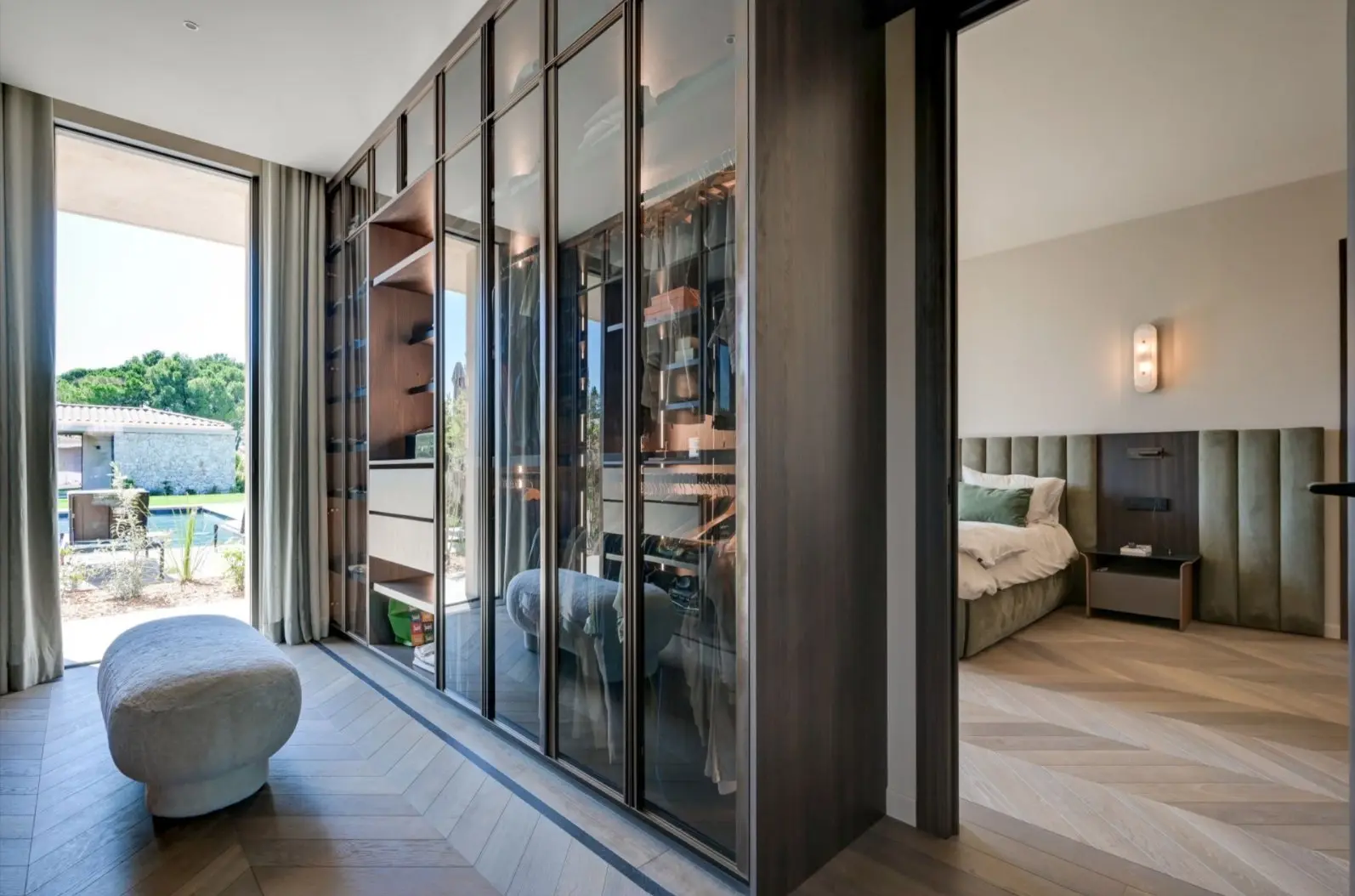 Chambre de la Villa F. : verrière en bois foncé, tête de lit capitonnée et accès au jardin