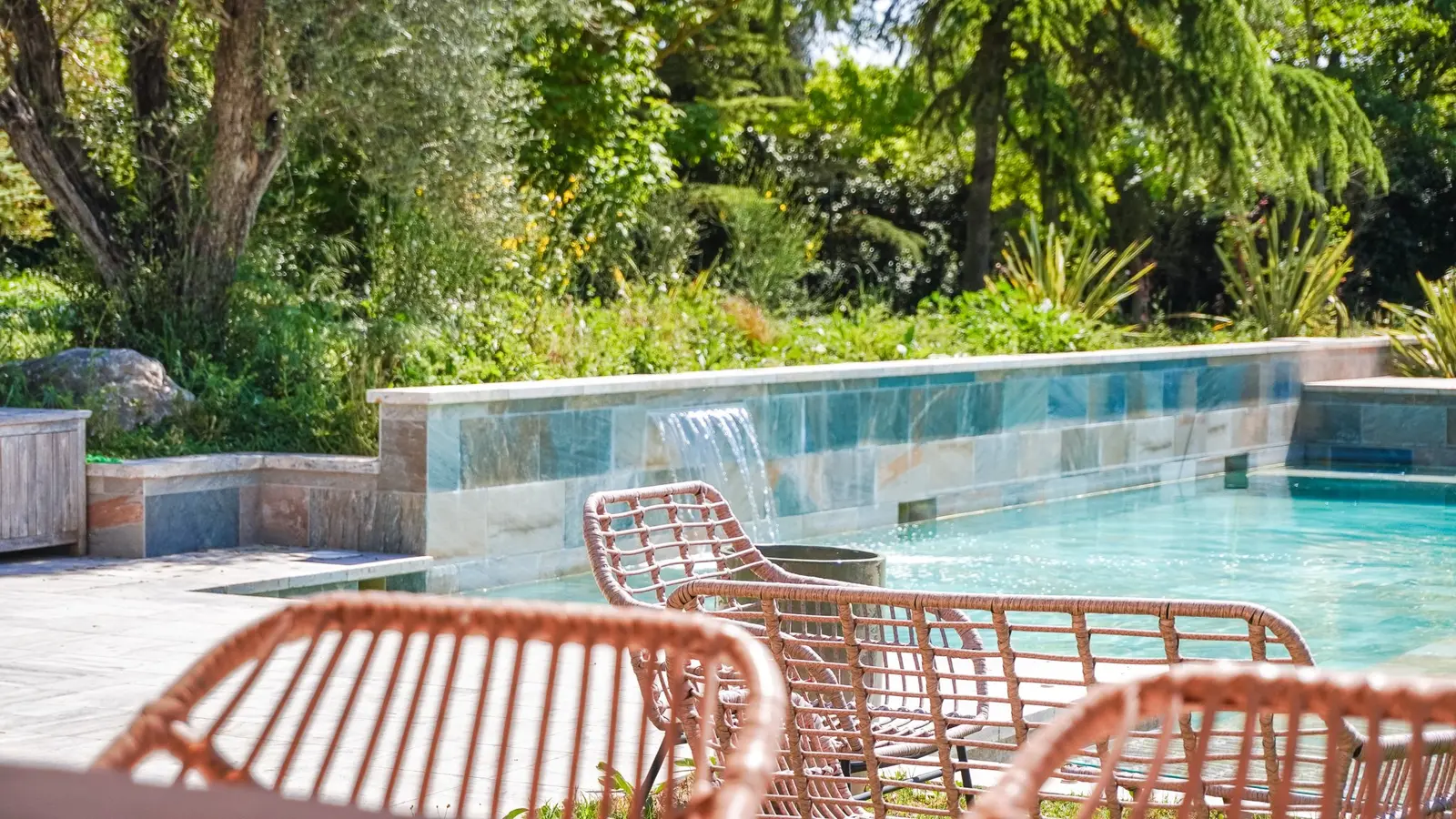 Fontaine en pierre au bord de la piscine, fauteuils en rotin, Villa S.