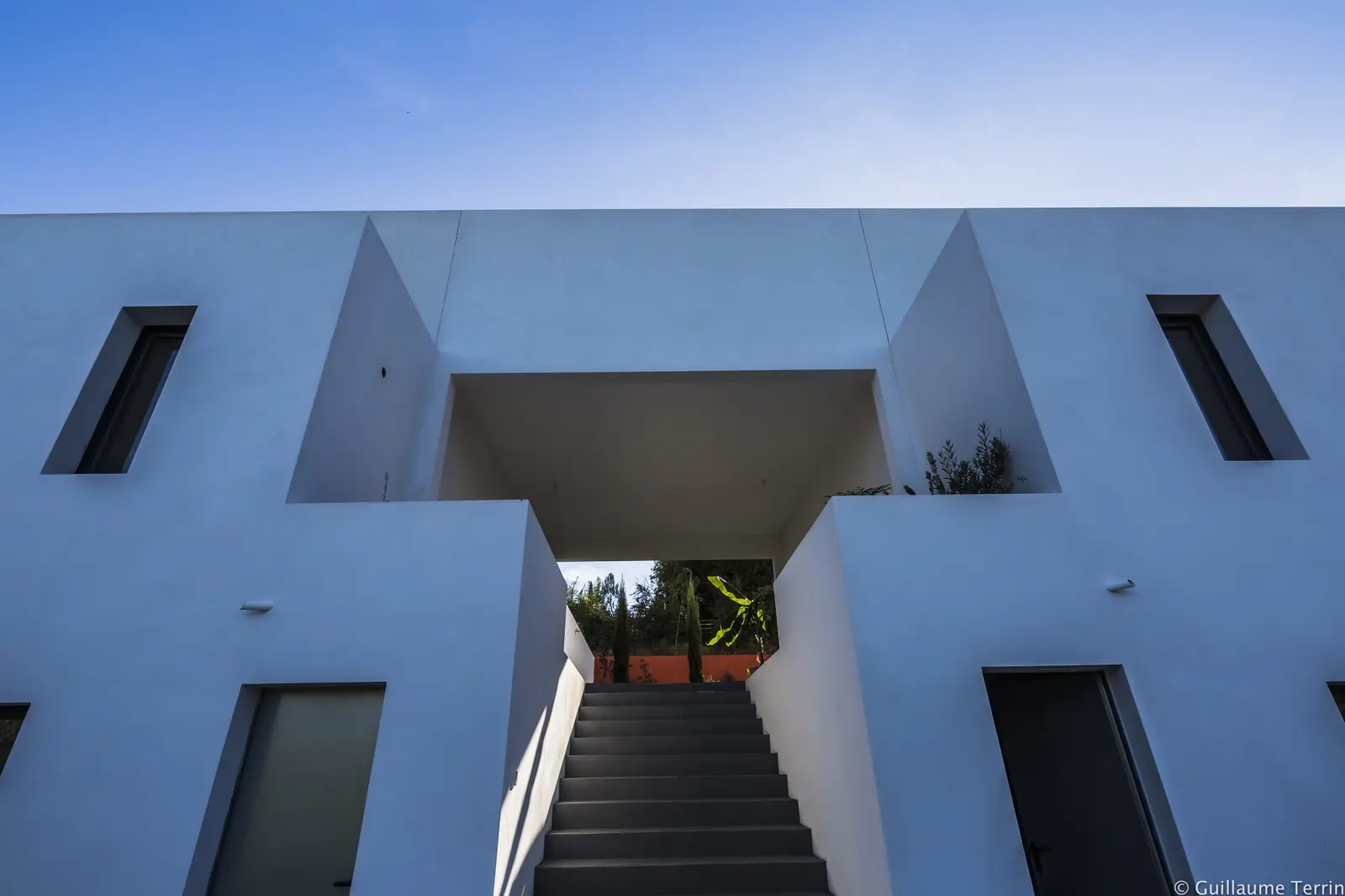 Façade blanche de la Villa T. : porche et escalier entre deux volumes